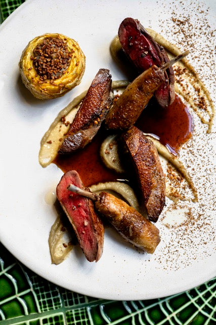 Assiette de viande grillée accompagnée de purée, d'une sauce brune et d'un légume farci, présentée sur une table ornée d'un napperon vert.