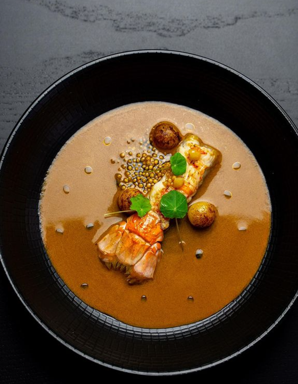 Langoustine immergée à moitié dans une sauce se rapprochant d'une bouillabaisse 