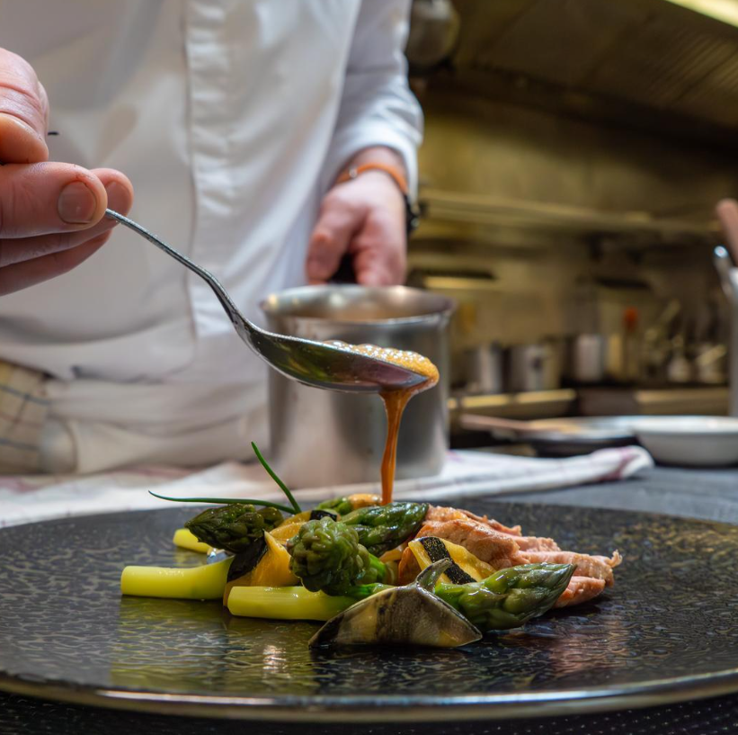 Chef qui dresse de la sauce sur une assiette printanière avec des asperges vertes et de la viande rosée