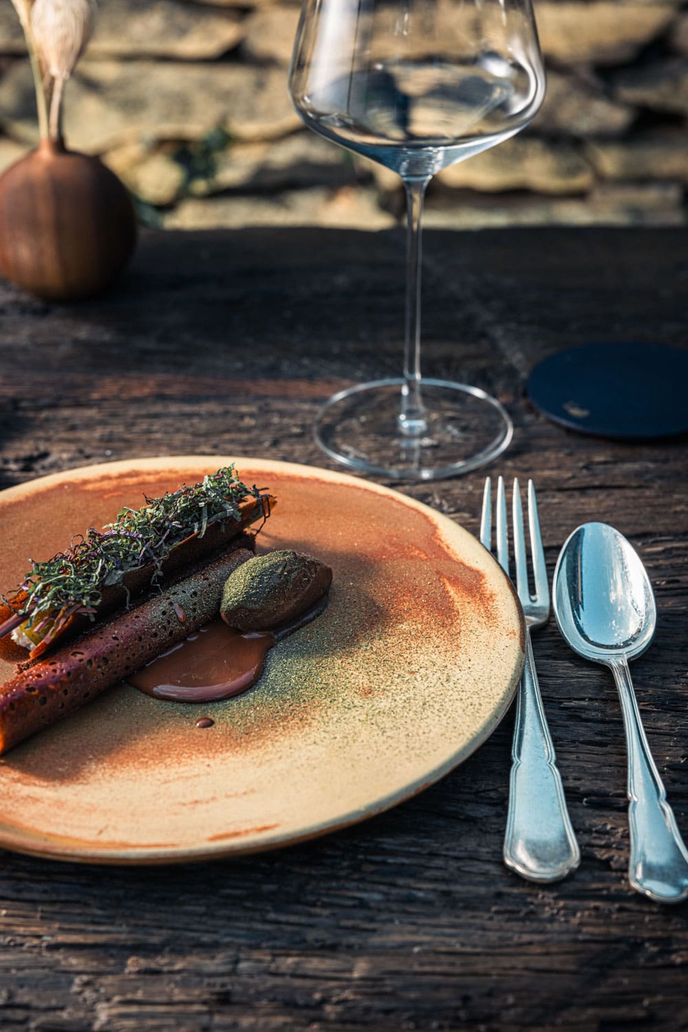 Assiette gastronomique avec plusieurs pièces de viande, des sauces et une décoration soignée, accompagnée d'un verre de vin rouge sur une table en bois rustique