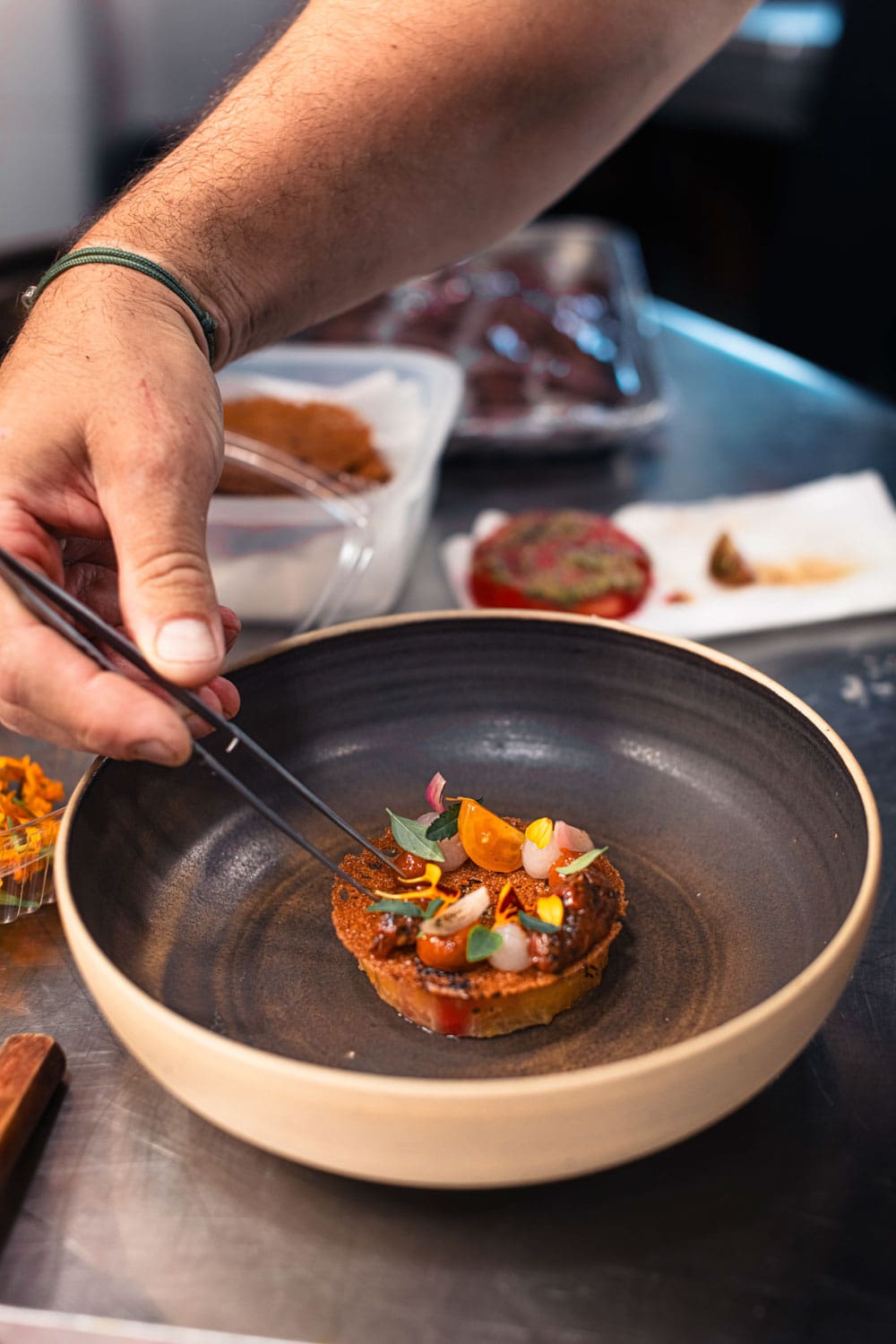 Main versant une sauce rouge sur un plat de présentation gastronomique avec une lampe à huile et des éléments décoratifs en arrière-plan
