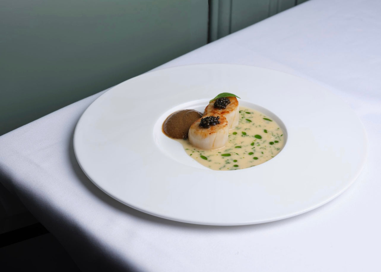 Assiette élégante avec des coquilles Saint-Jacques dans une sauce crémeuse, garnie de caviar et accompagnée d'une purée de champignons.