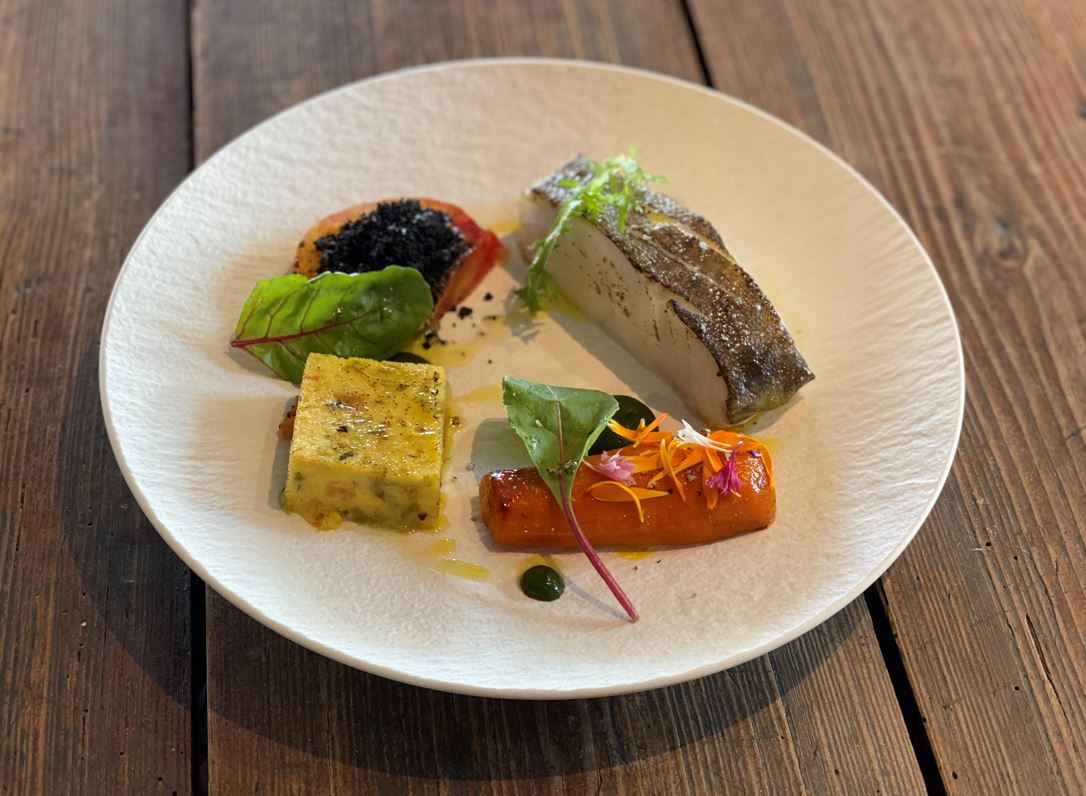 Assiette gastronomique avec poisson grillé, légumes colorés, carré de flan salé et garnitures artistiques.