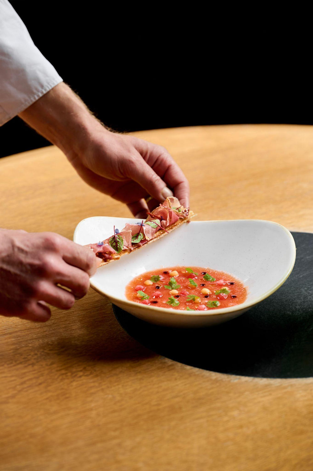 Bol de soupe froide rouge avec des morceaux de légumes et des herbes, accompagné de tranches de jambon sur du pain