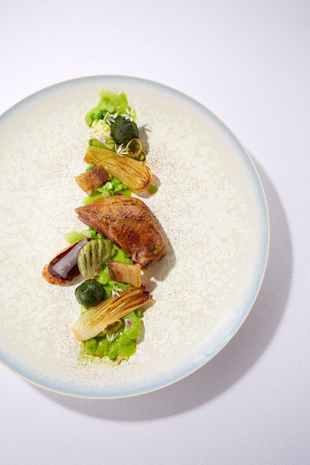 Plat gastronomique avec viande rôtie et légumes verts, présenté sur une assiette blanche