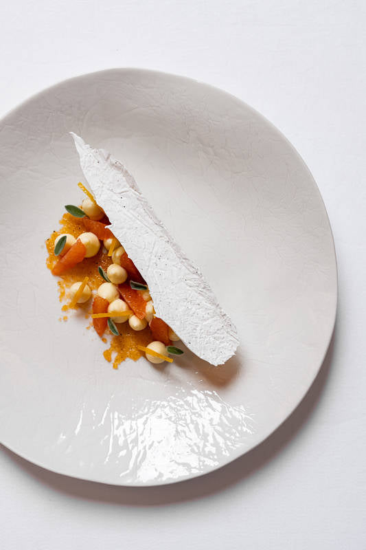 Assiette gastronomique élégante avec une présentation artistique de légumes et de sauce, surmontée d'une fine feuille croquante blanche.