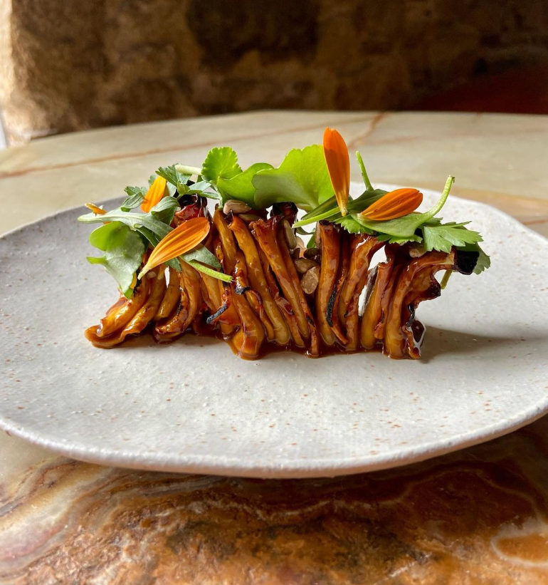 Assiette de champignons caramélisés, décorée de fleurs comestibles et de fines herbes.