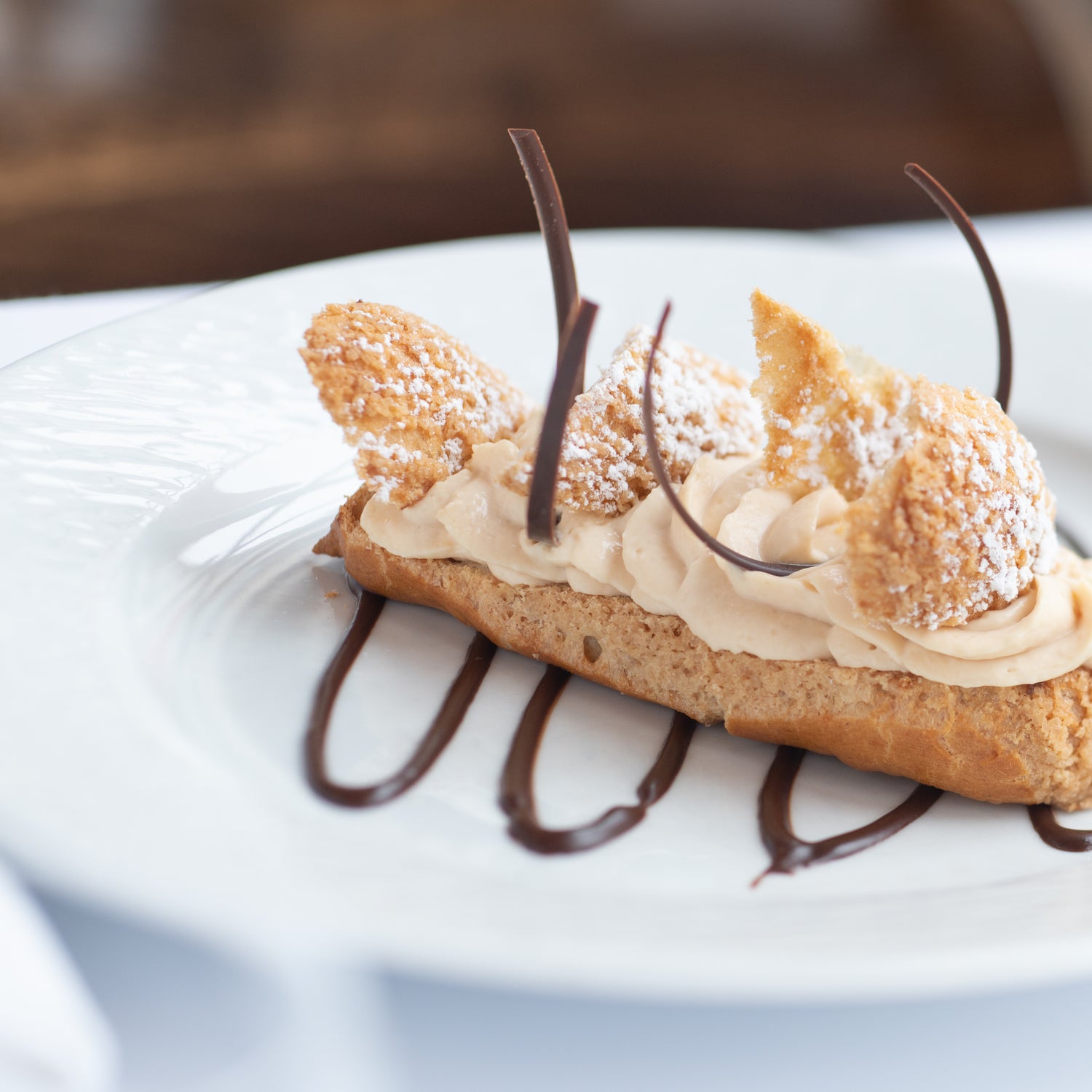 Éclair délicatement présenté, garni de crème légère et décoré de motifs en chocolat et de sucre glace, sur une assiette blanche.