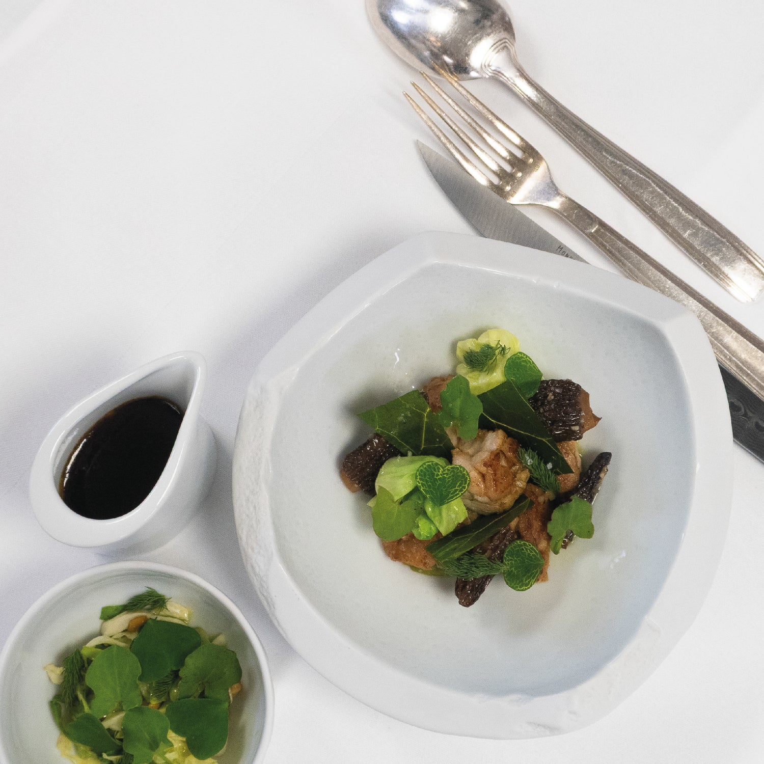 Ris de veau croustillant dressé avec morilles et jeunes pousses, accompagné de sauce et garniture dans de petits bols.