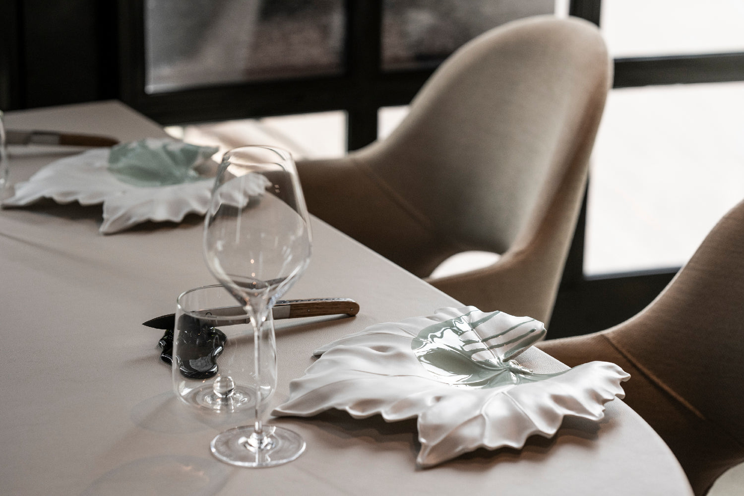 Table dressée du restaurant Arbane avec verres à vin et assiettes en forme de feuille en porcelaine blanche.