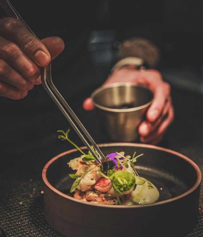 Chef arrangeant un plat de fruits de mer avec précision, ajoutant des herbes avec des pinces.