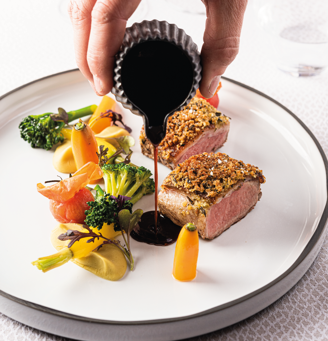 Service d'une sauce noire sur un filet croustillant accompagné de légumes colorés et brocolis