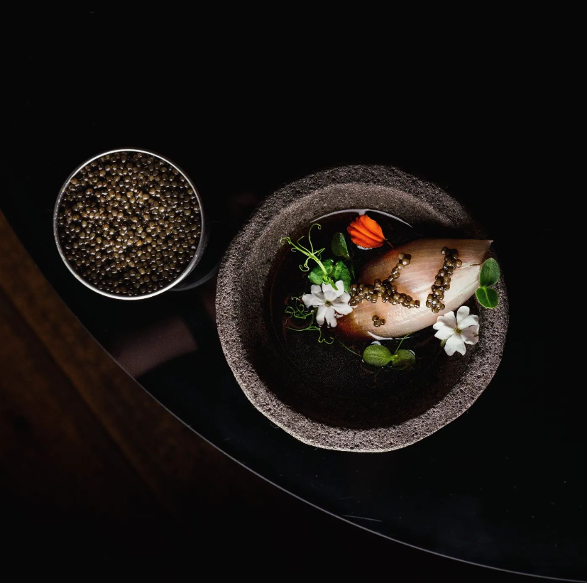 Assiette avec une préparation artistique de poisson, caviar et fleurs comestibles.