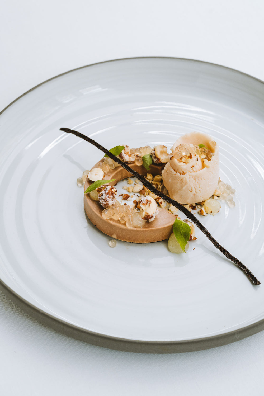 Dessert raffiné composé de foie gras, noisettes caramélisées, perles de saveur et une gousse de vanille sur une assiette blanche.
