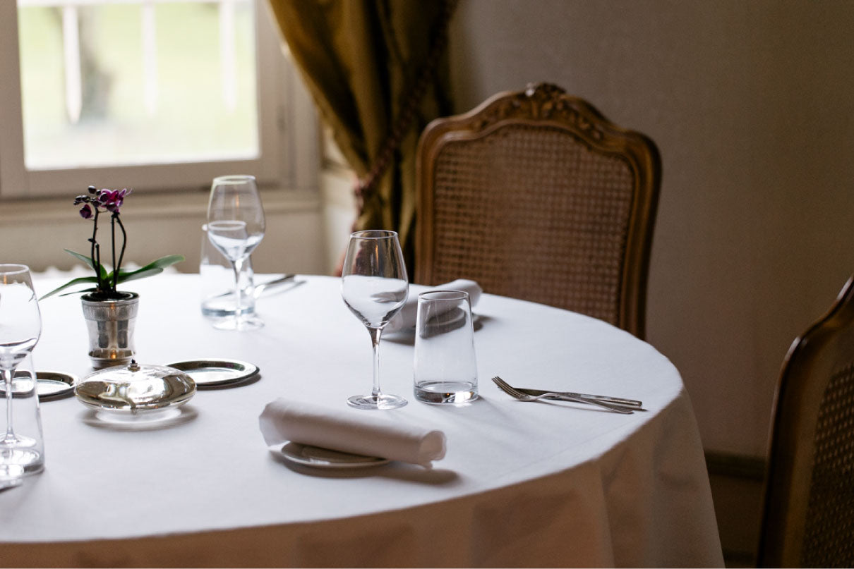 Table élégamment dressée dans un salon raffiné avec nappe blanche, verrerie fine et chaise en bois sculpté.