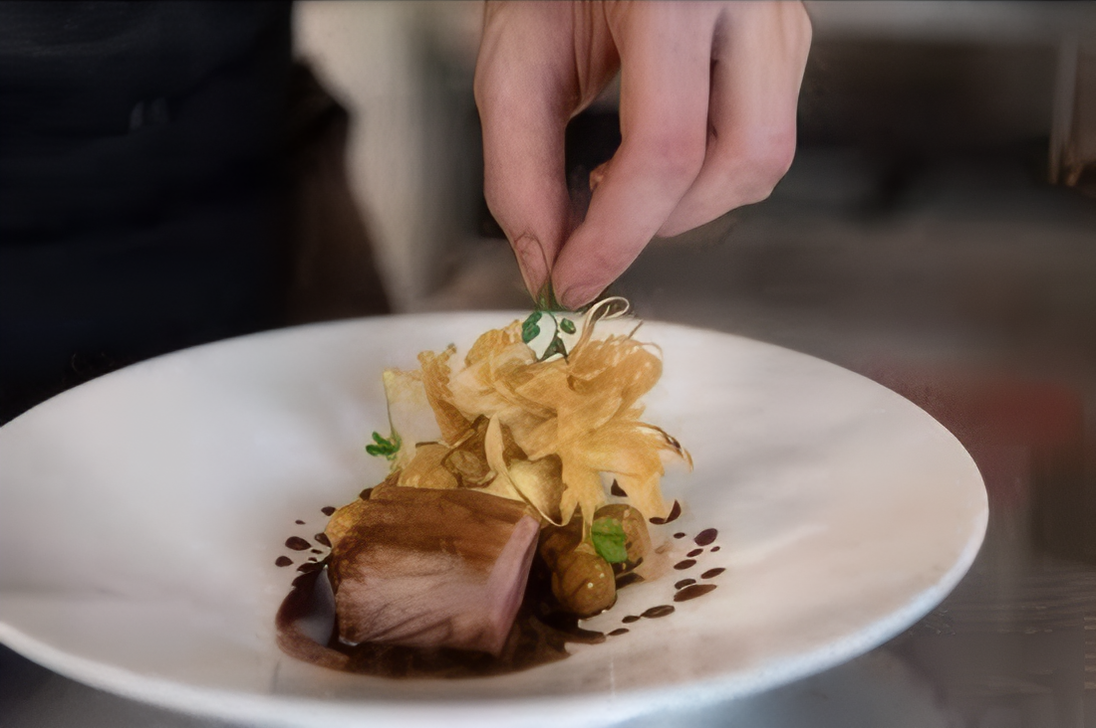 Chef en train de finaliser un plat gastronomique avec une touche délicate sur une assiette soigneusement dressée.