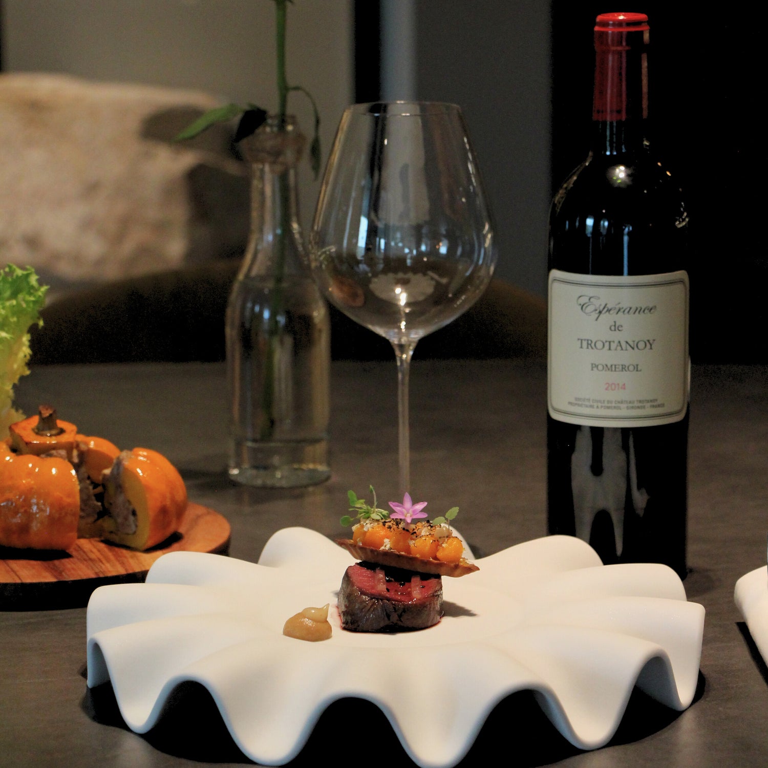 Plat de viande gourmet servi dans une assiette design, accompagné d’un verre et d’une bouteille de vin rouge, sur une table élégante.