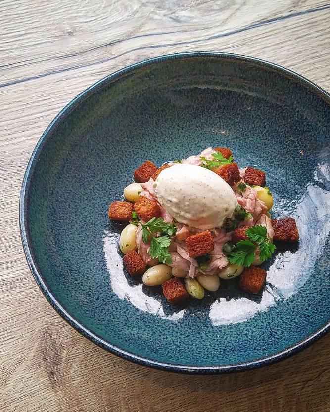 Salade composée de morceaux de viande, croûtons dorés et haricots, surmontée d'une quenelle de crème.






