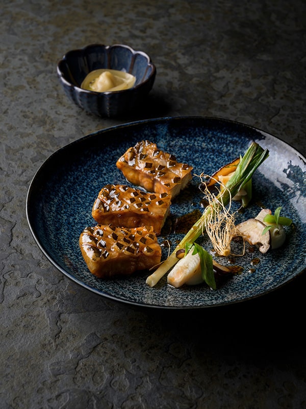 Préparation raffinée de légumes et viande sur une assiette bleu foncé texturée
