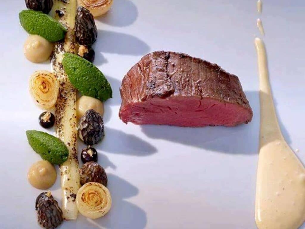 Plat gastronomique avec filet de viande rouge, morilles, purées colorées et sauce élégamment dressée.