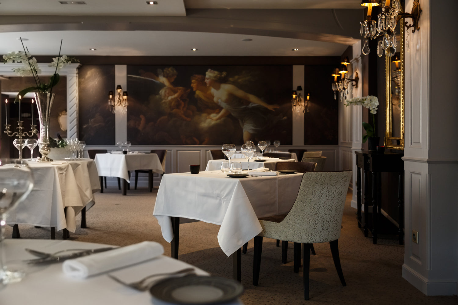 Restaurant élégant avec des tables dressées et une fresque murale.