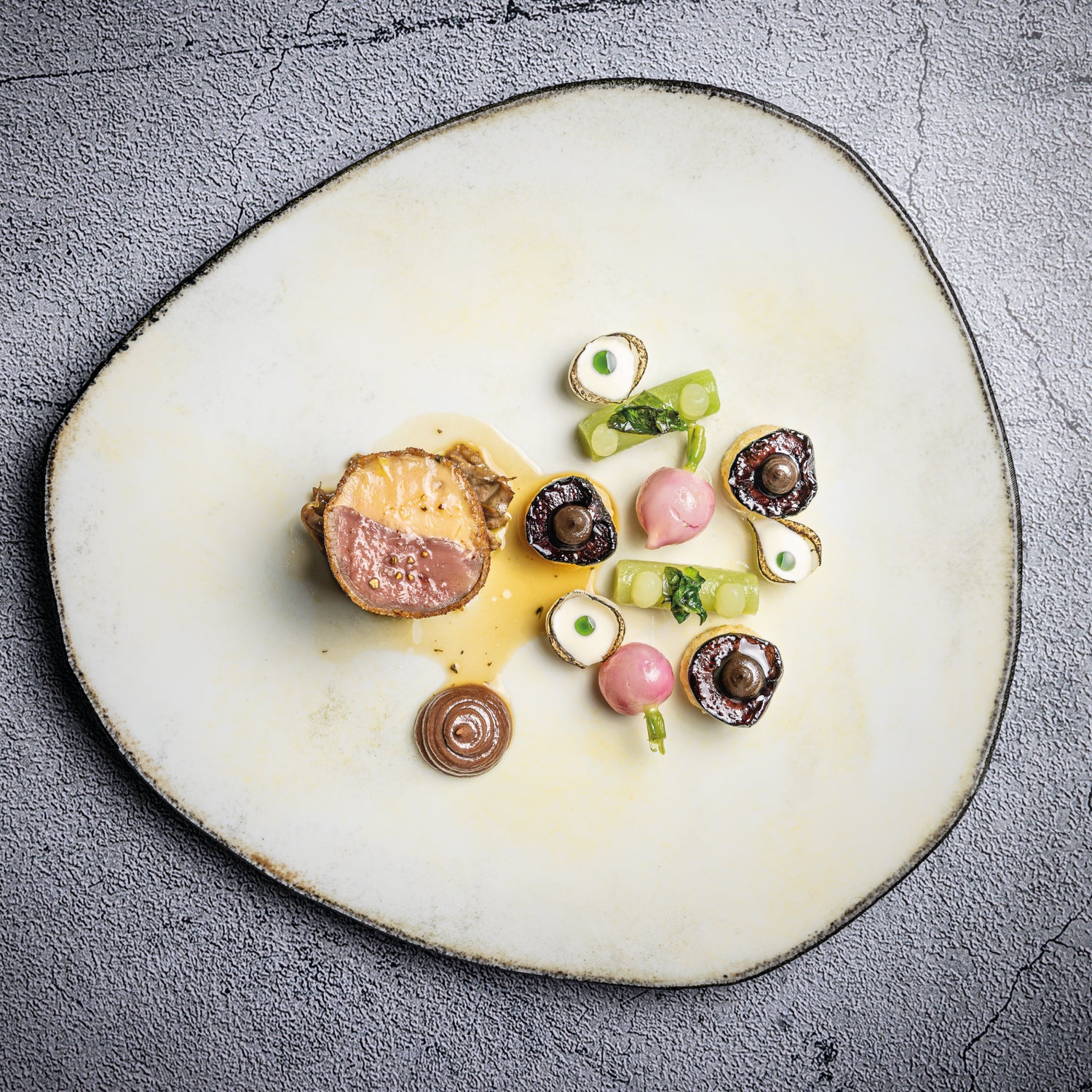 Présentation artistique d'un plat gastronomique comprenant une pièce de viande tendre accompagnée de légumes soigneusement disposés et de sauces élégantes, le tout sur une assiette texturée.