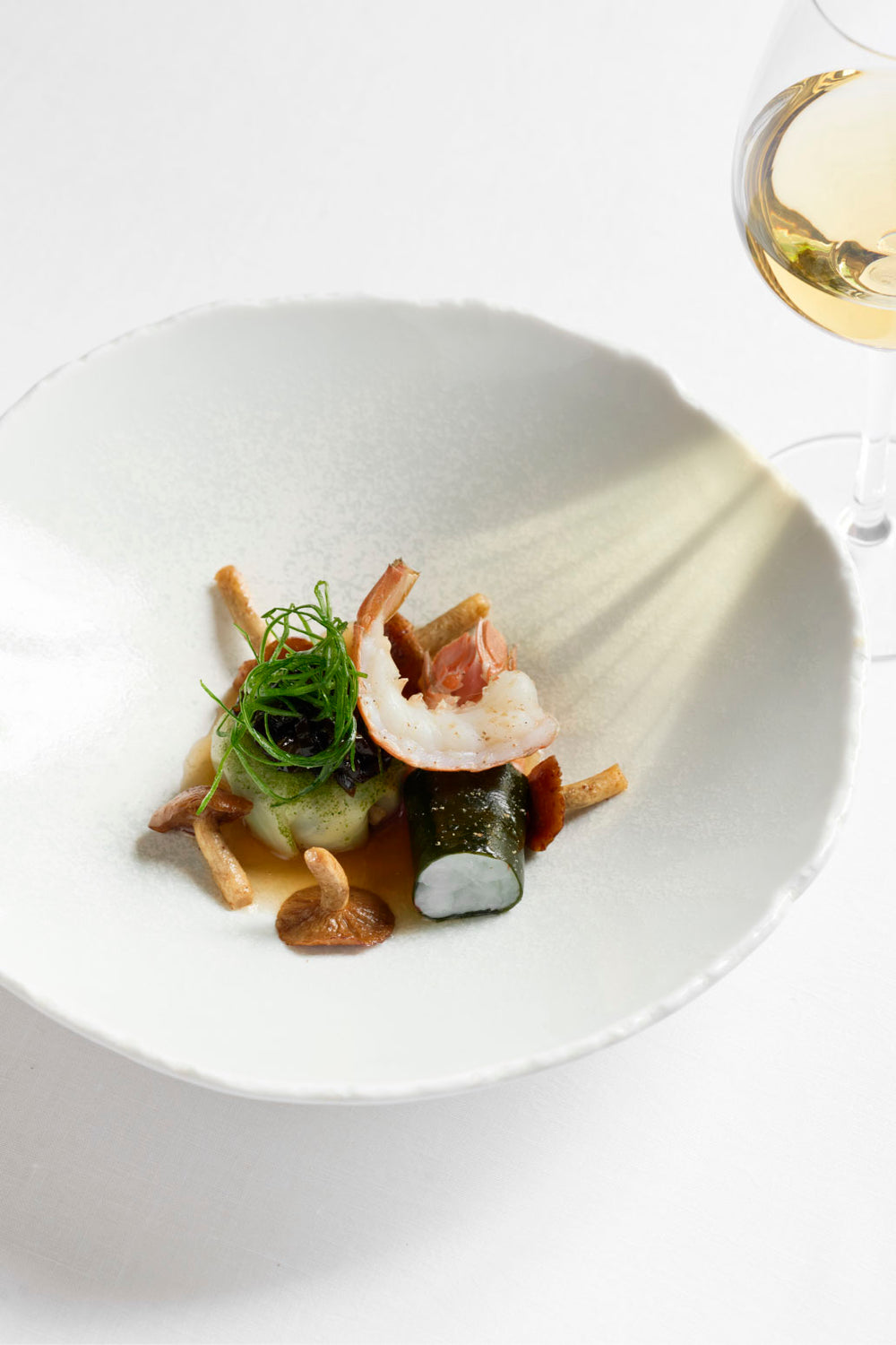 Plat gastronomique de langoustine accompagnée de légumes et champignons, dressé avec finesse dans une assiette blanche.