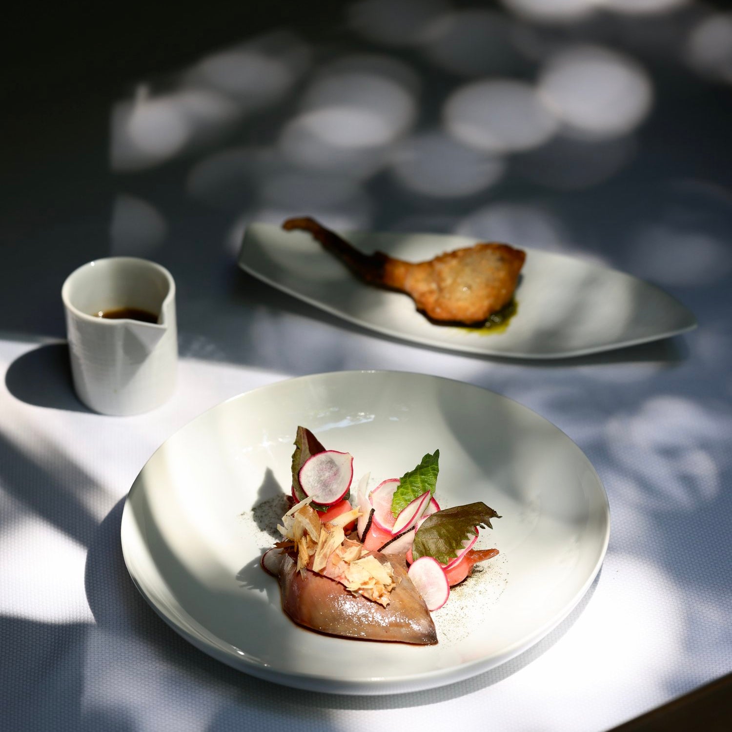 Plat raffiné avec légumes et viande, éclairé par des ombres d'arbres pour une présentation artistique.
