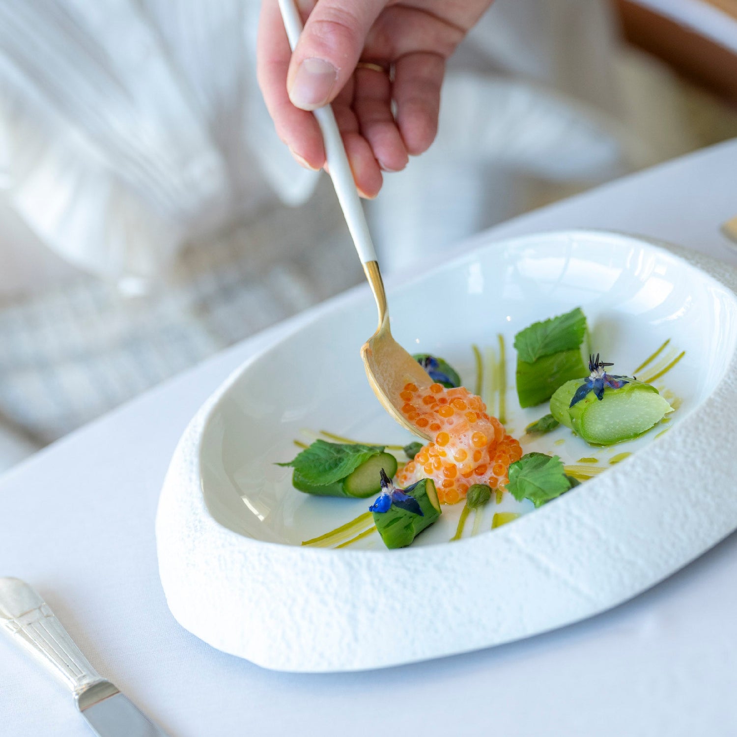 Plat gastronomique avec des perles de saumon, des garnitures vertes et des fleurs comestibles, servi dans une assiette blanche.