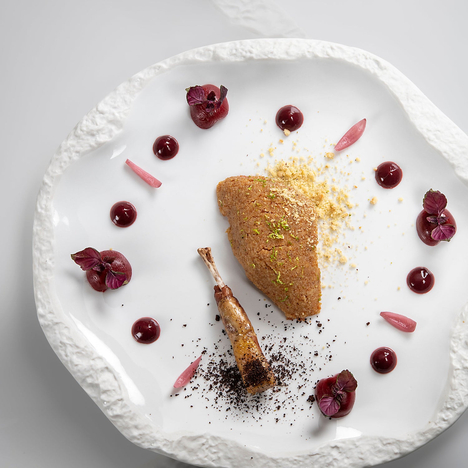 Plat gastronomique disposé artistiquement dans une assiette blanche, avec des garnitures et des sauces colorées.