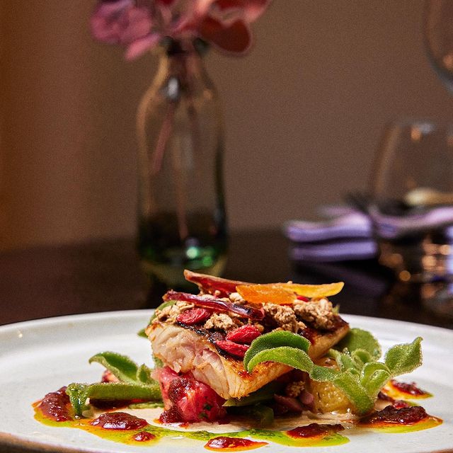 Un plat sophistiqué de poisson, accompagné de légumes verts et décoré avec des pétales de fleurs comestibles.