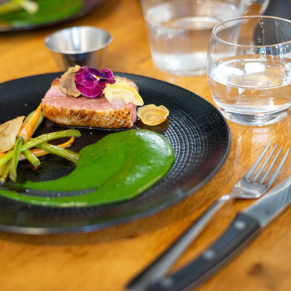 Assiette élégante avec du foie gras décoré de fleurs comestibles violettes et accompagné d'une sauce orange, servie avec une tranche de pain grillé.