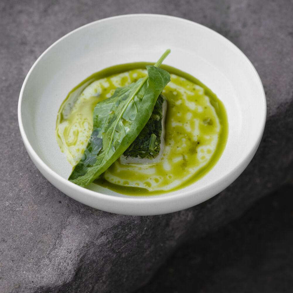 Un plat de légumes verts et de sauce verte, garni de feuilles d'épinard, présenté dans une assiette blanche.
