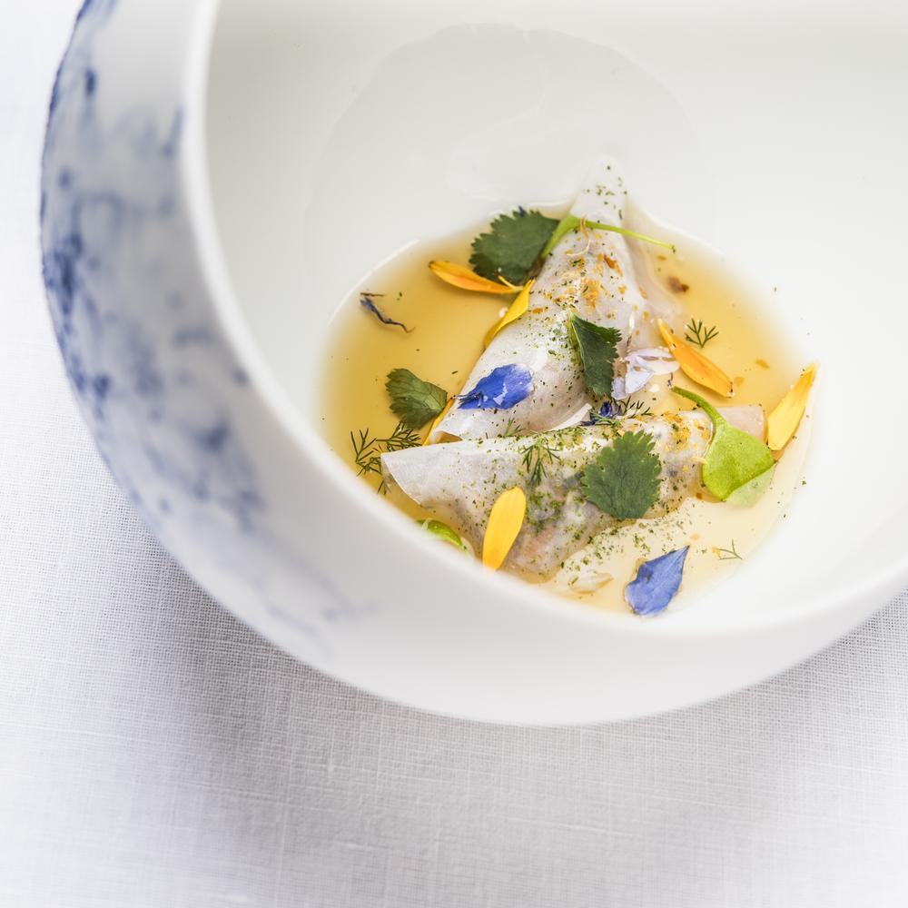 Un plat gastronomique avec des ravioles garnies de fleurs et d'herbes, servies dans un bouillon clair.