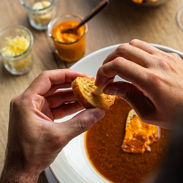 Un bol de soupe ou de sauce, avec une personne trempant un morceau de pain dedans, une scène qui met en avant le plaisir de manger.