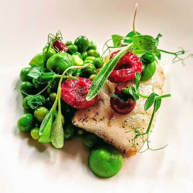 Assiette de poisson avec des petits pois et des framboises, offrant un contraste de couleurs vives