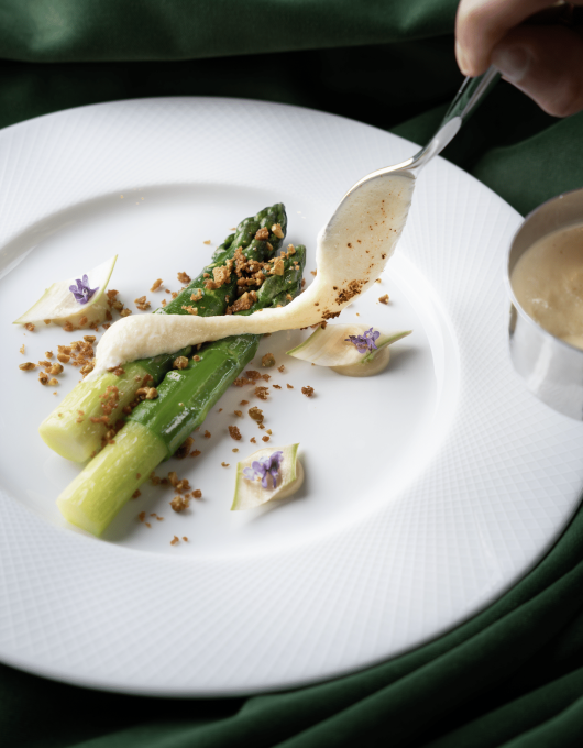 Asperges avec sauce et garniture sur assiette blanche.